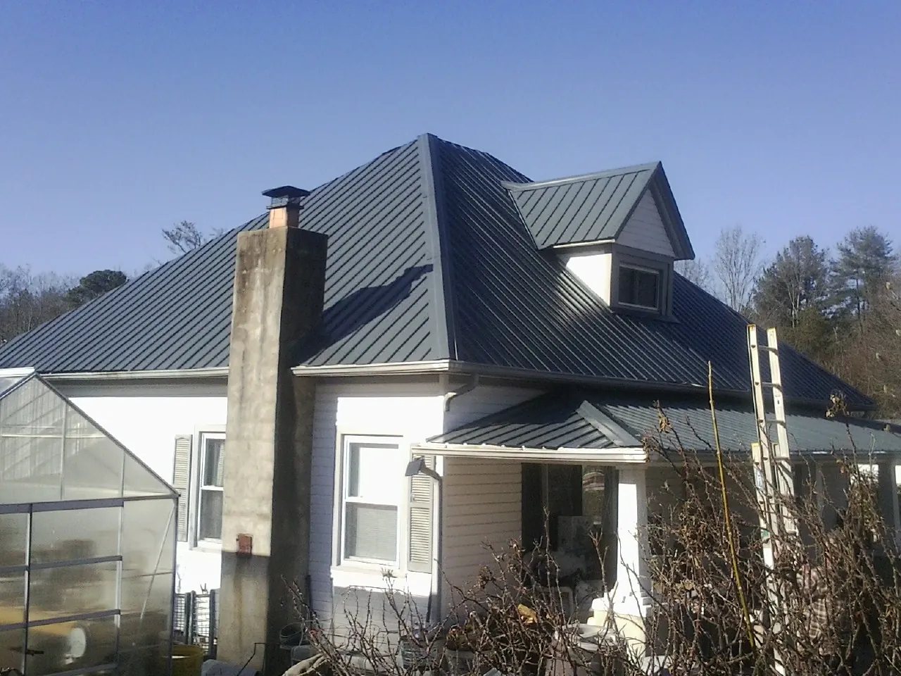 Dark blue standing seam metal roof on a white farmhouse with dormer — Slate & Tile Roof Repair by Roofing Brothers in Lake Preston