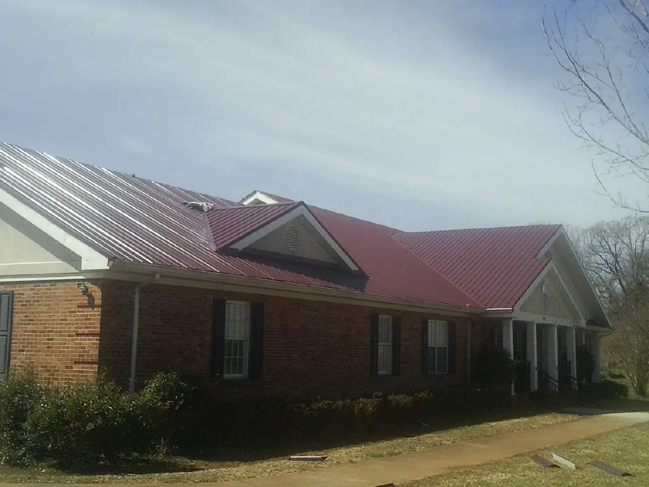 Red metal roof with gabled entries on a long brick building, from a Hail Damage Roof Repair job in Lake Preston