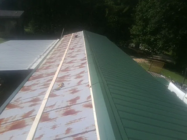 Old rusted panels beside newly installed green metal roofing — Wind Damage Roof Repair by Roofing Brothers in Lake Preston