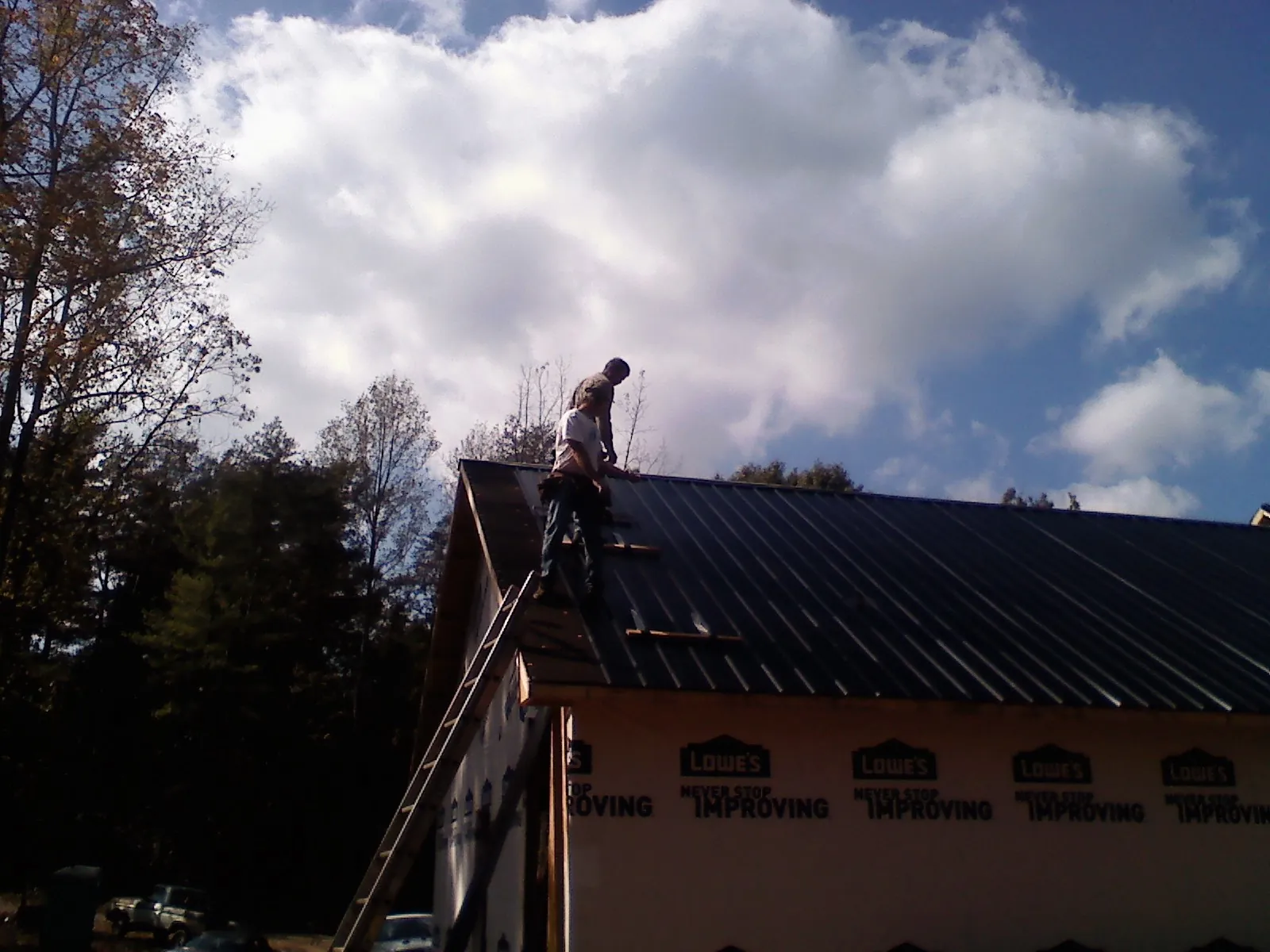 Roofer fastening dark metal panels high against a cloudy sky, from a Roof Inspection job in Lake Preston