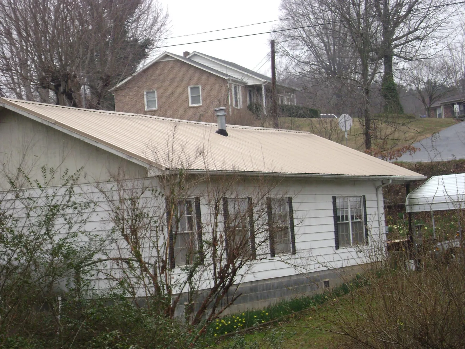 Tan metal roof on a white sided house set into a hillside — Commercial Roofing by Roofing Brothers in Lake Preston