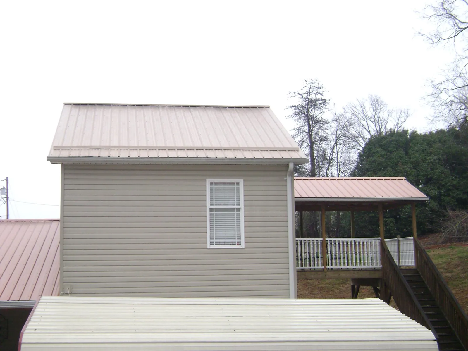 Tan metal roofs on a two story addition and attached porch, from a Roof Replacement job in Lake Preston
